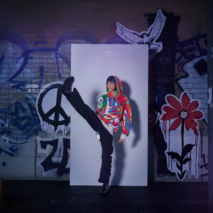 Frau steht vor einer Graffiti Wand und trägt den 17 Ziele Hoodie